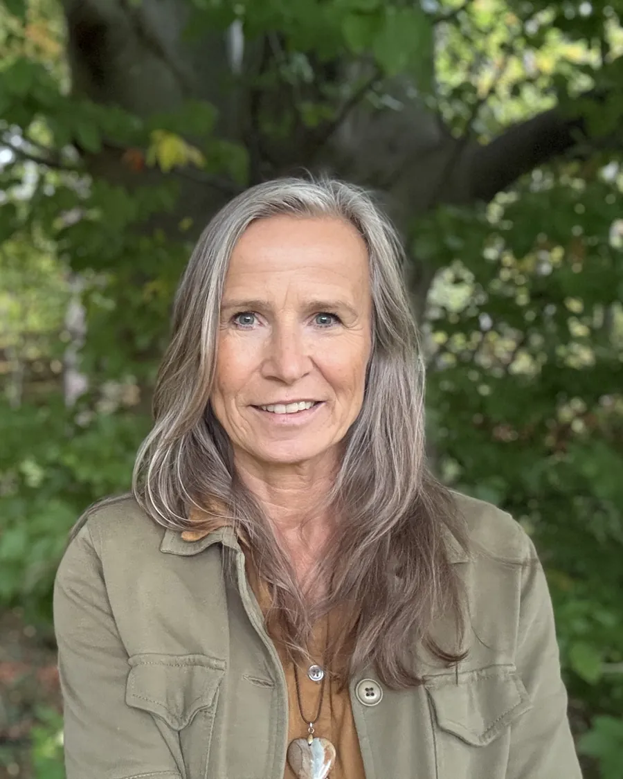 Grazyna von Lonski lächelt im Wald, hinter ihr der Stamm einer großen Buche