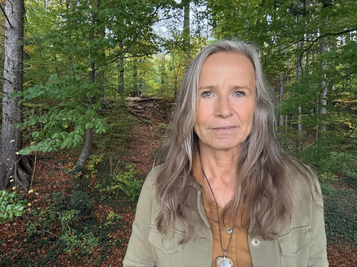 Grazyna von Lonski mit ruhigem Blick im Wald, hinter ihr ein Waldweg