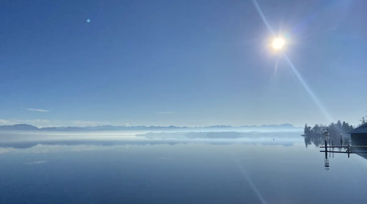 Die Sonne spiegelt sich im ruhigen, klaren Wasser des Sees