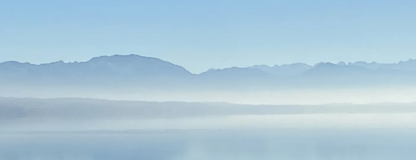 Berge in Schichten aus blauem Dunst über einem spiegelglatten See