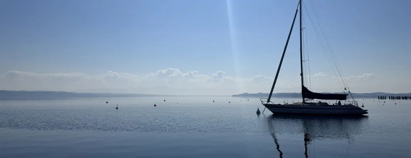 Ein Segelboot liegt ruhig vor Anker auf dem stillen See, ein Lichtstrahl fällt vom Himmel
