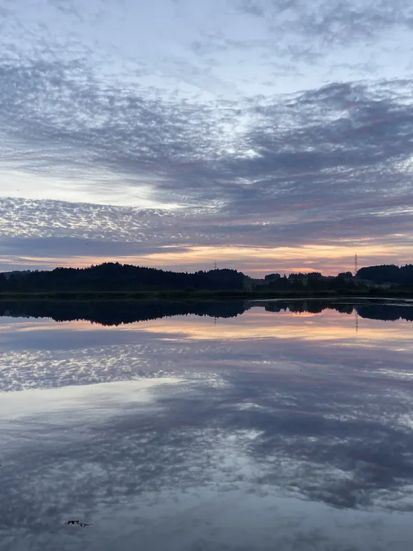 Ein Schäfchenwolkenhimmel spiegelt sich so vollkommen im stillen See, dass oben und unten kaum zu unterscheiden sind